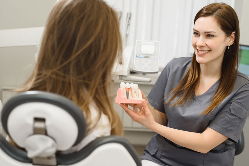 image of a dental professional showing a patient a dental implant model for her affordable dental implant treatment