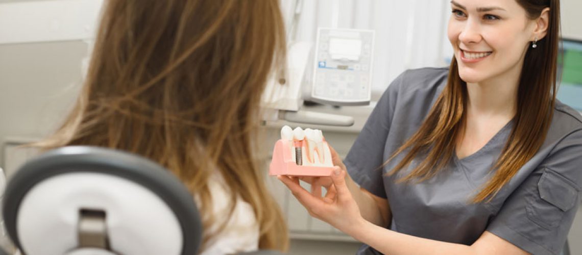 image of a dental professional showing a patient a dental implant model for her affordable dental implant treatment